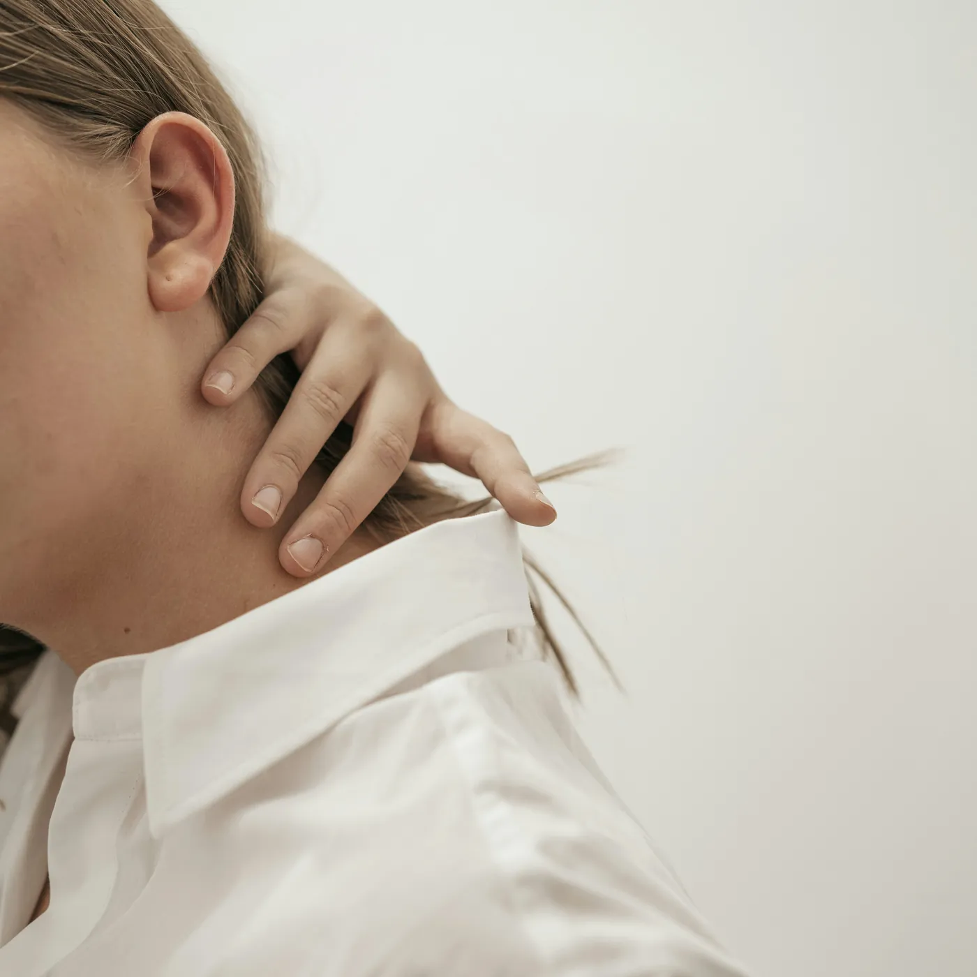 Woman in a white shirt resting a hand at the back of her neck